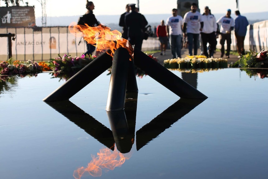 The Kings Park flame of remembrance burns in daylight with people in the background.
