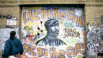 Mural of Tupac on garage door with words 'Live by the gun, die by the gun'.