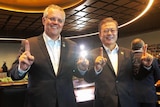 Two man in suits standing next to each other, holding up their index fingers