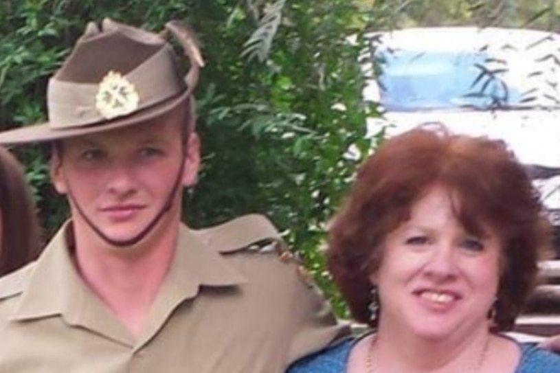 A young man in an army uniform poses with his arm around the shoulder of an older woman.