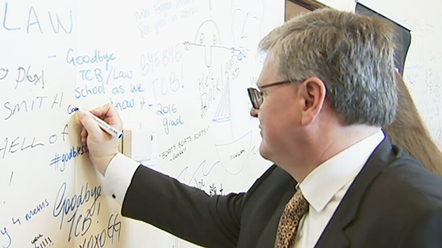 Man in suit writes on wall full of graffiti at the University of Queensland