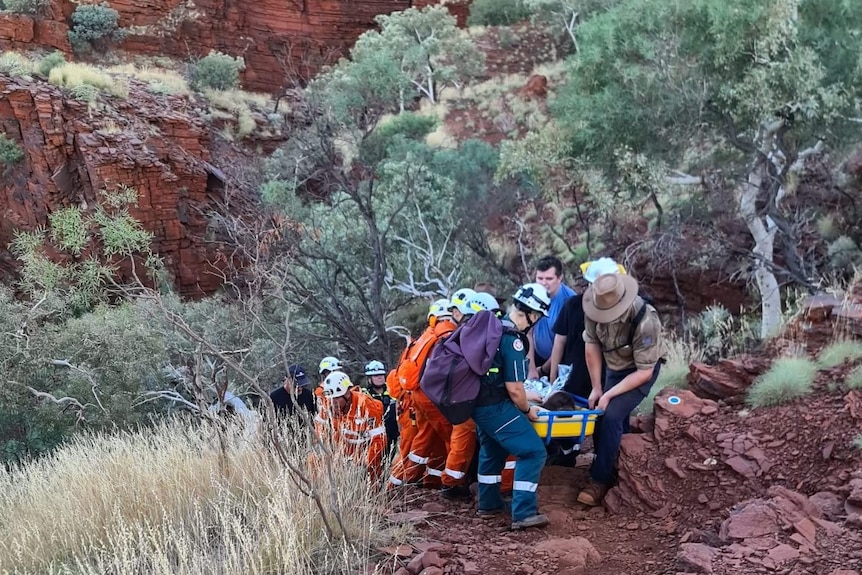 A group of people help carry a woman in a stretcher up a steep, rocky hill.