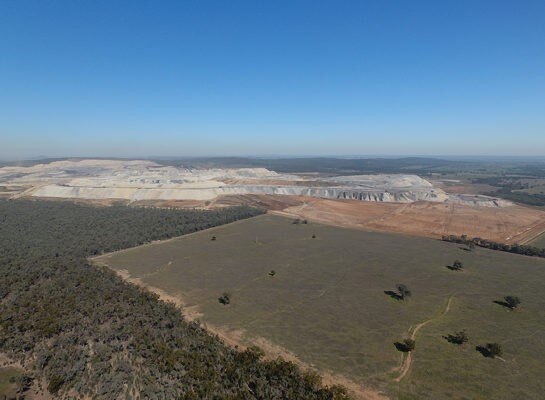An image from the air of an open cut mine, next to forest and a paddock