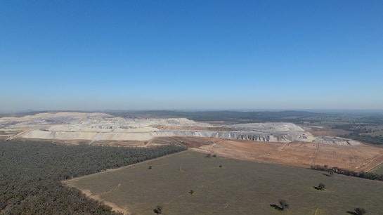 An image from the air of an open cut mine, next to forest and a paddock