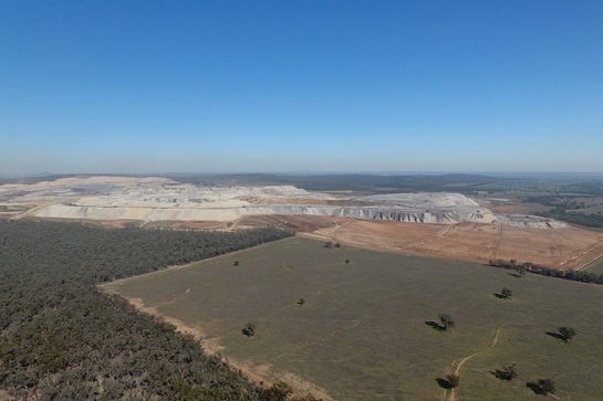 An image from the air of an open cut mine, next to forest and a paddock