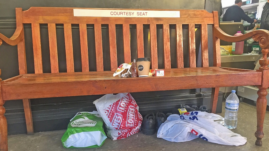 A curtesy seat inside a supermarket with plastic bags and shoes underneath it.