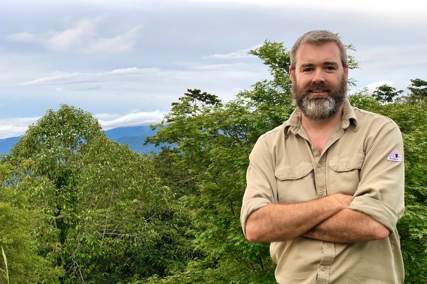 a man stands near a forest looking into camera