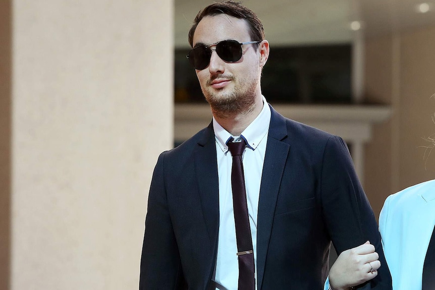 A young man in a suit and sunglasses holding an unseen woman's arm