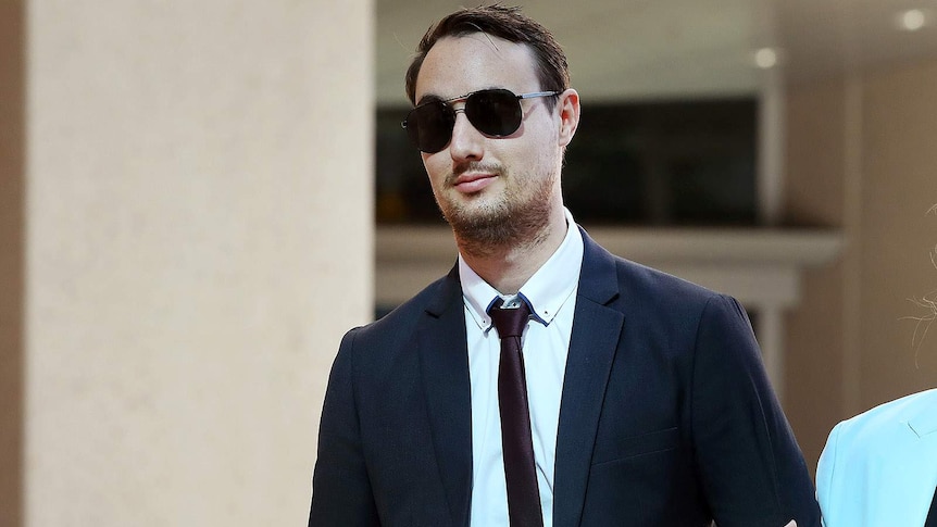 A young man in a suit and sunglasses holding an unseen woman's arm