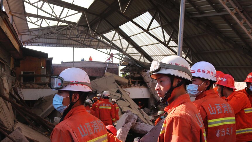 Rescue workers in high-vis orange overalls and hardhats work to remove rubble