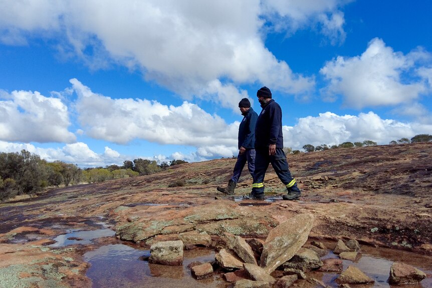Two men in fire uniforms walk through a rocky area in the outback.