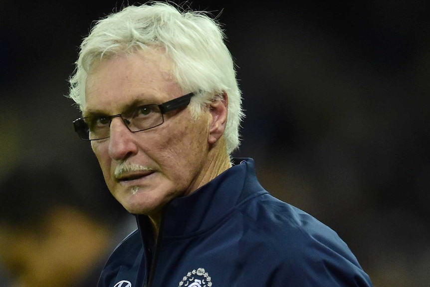 Mick Malthouse wearing glasses and a team tracksuit and looking grumpy.