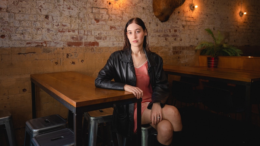 Harriette poses cross-legged at a table in an empty bar