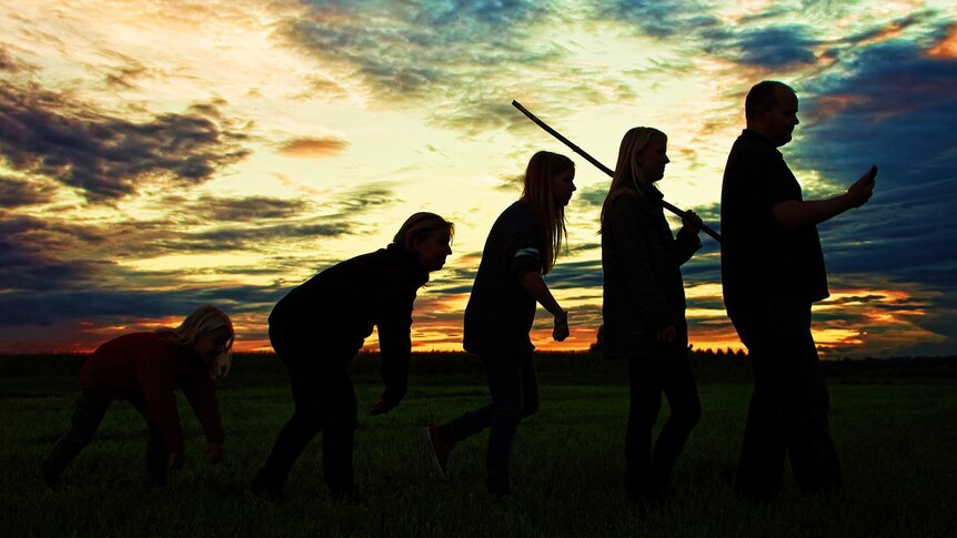 Five people walk across a field in a modern representation of the ascent of man and evolution.