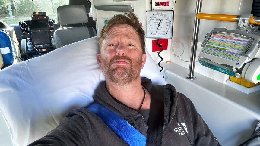 A white man taking a selfie looking in pain in the back of an ambulance.