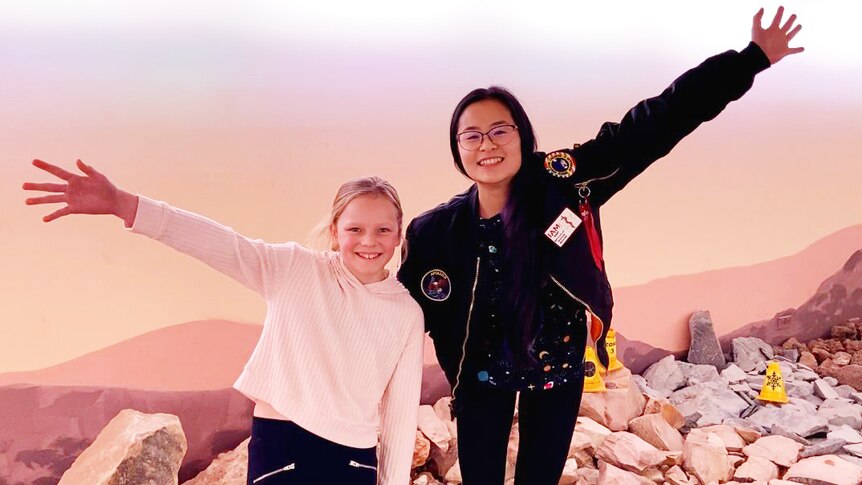 A girl and young woman pose for a photograph in a room simulating the surface of Mars.