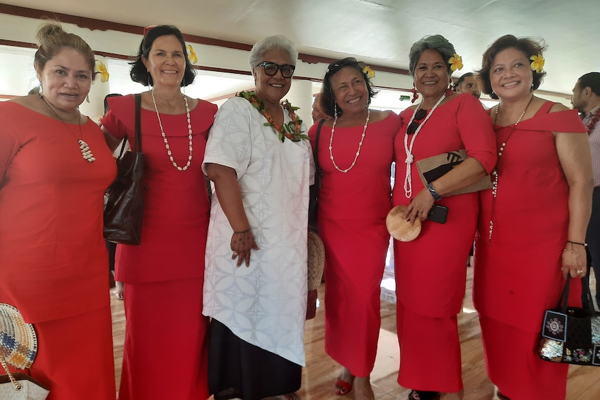 Five women dressed in red flank one woman dressed in white. 