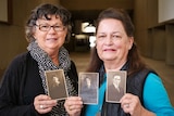 Two ladies holding black and white photos.