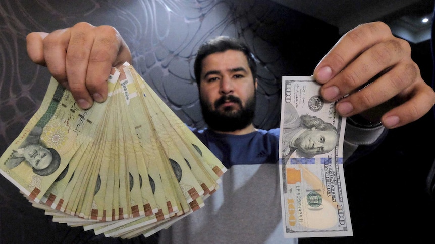 Money changer poses with US dollar and Iranian rials