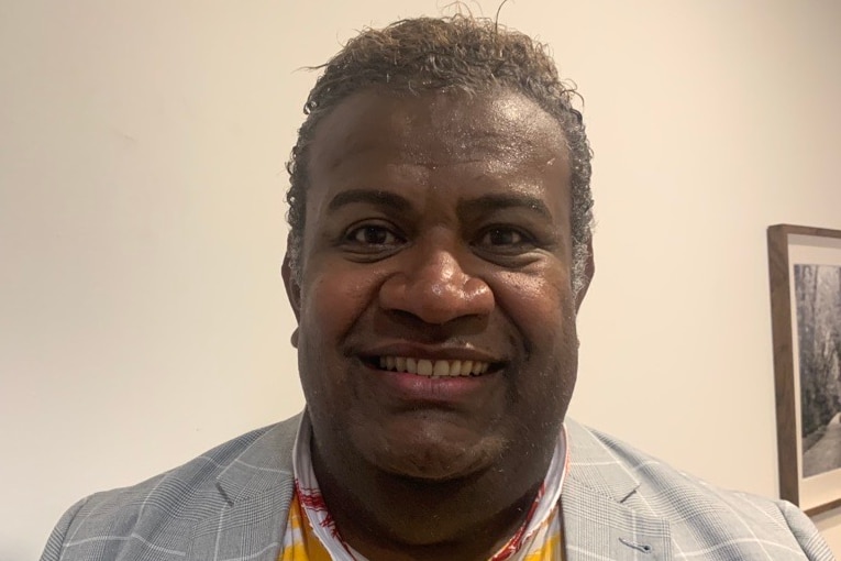 A fijian person with short curly hair smiling in a room.