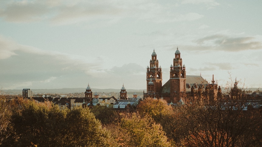 A landscape of tree canopies gives way to the rooftops of the city of Glasgow.