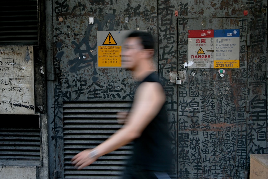 A man walks past an electricity box covered in black Chinese calligraphy.
