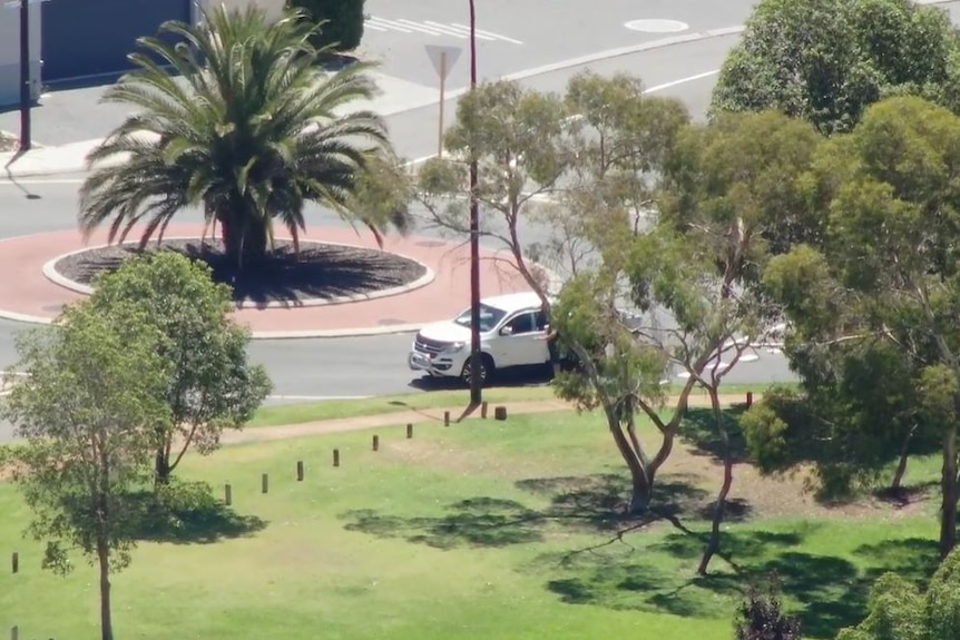 A white ute stopped at a roundabout while someone reaches for the door handle