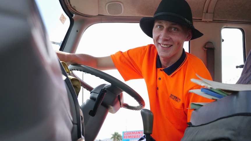 Nathan in the front of a truck, sitting in the drivers seat, steering wheel in front, wiping the dashboard.