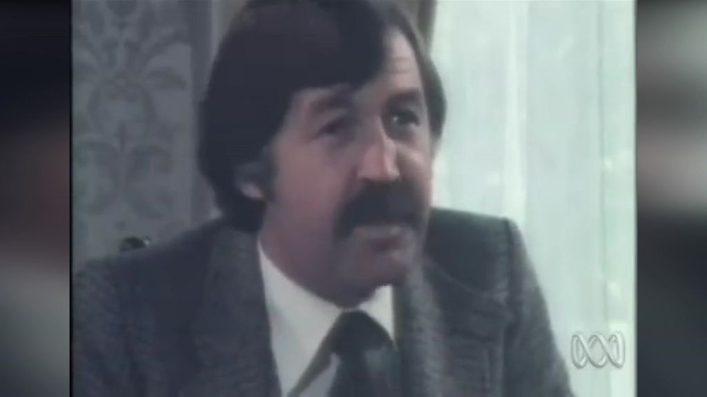 Archival footage of a man with brown hair and a brown moustache speaking while seated.