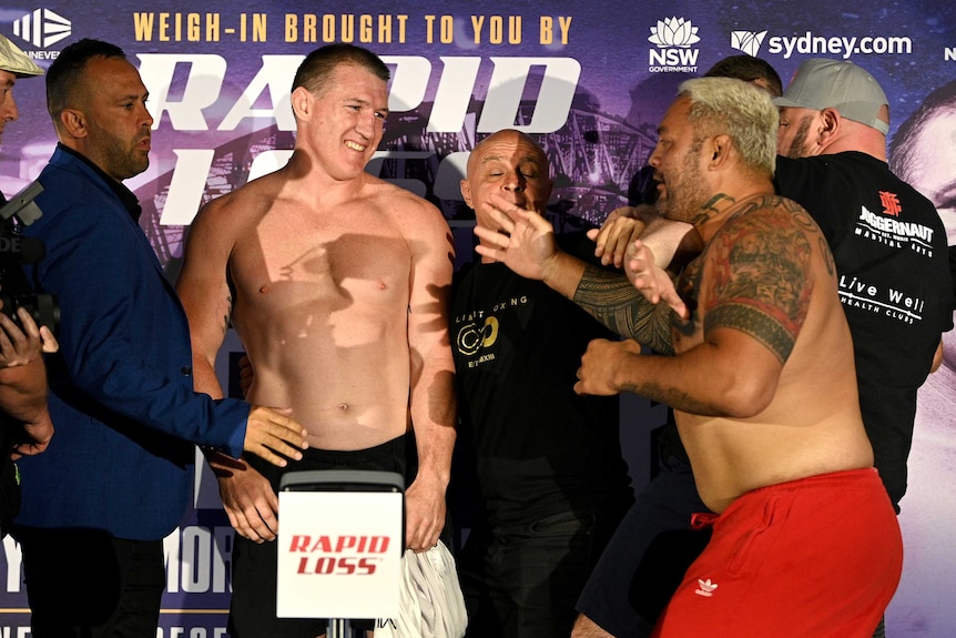 Paul Gallen smiles at Mark Hunt as he is held back by minders at a weigh-in before their boxing bout.