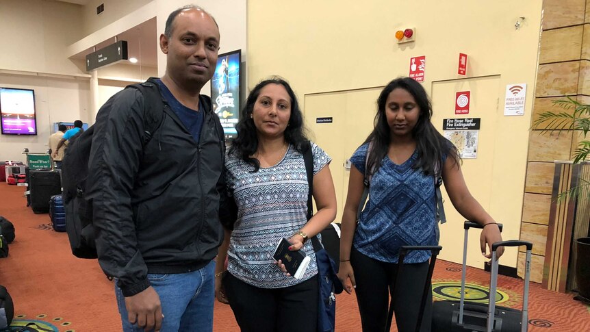 Naveen Henri stands with his wife and daughter at the baggage terminal.