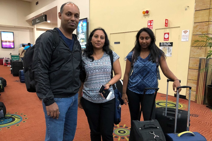 Naveen Henri stands with his wife and daughter at the baggage terminal.