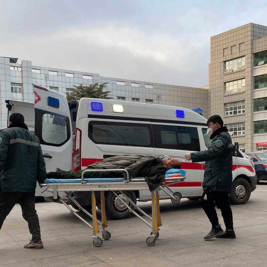 Medical workers push a man past an ambulance outside a hospital.