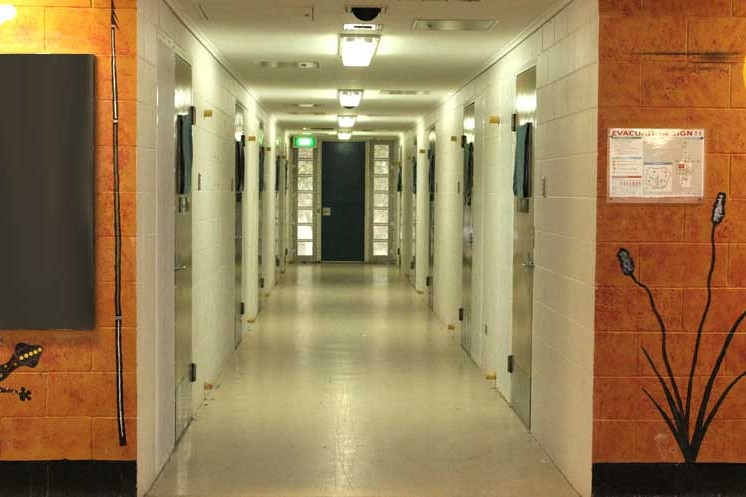 A long neon lit hallway with doors to cells.