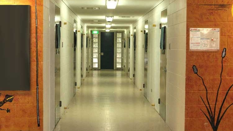 A long neon lit hallway with doors to cells.