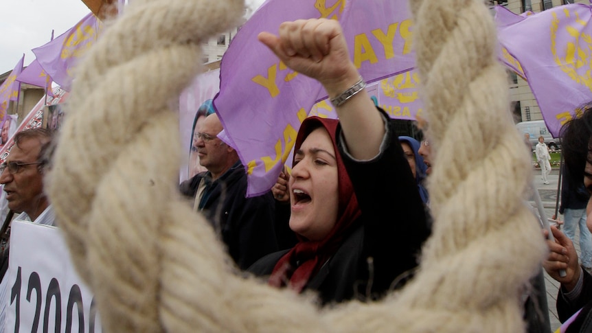 A woman protests behind a noose hanging in the street.
