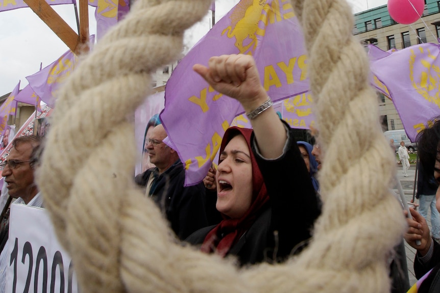 A woman protests behind a noose hanging in the street.