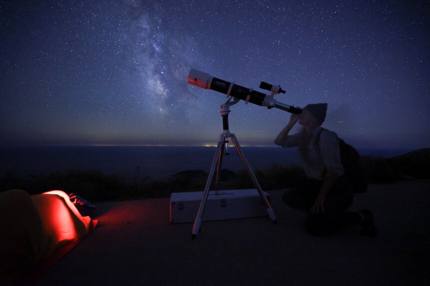 A woman looks through a telescope with a starry night sky in the background