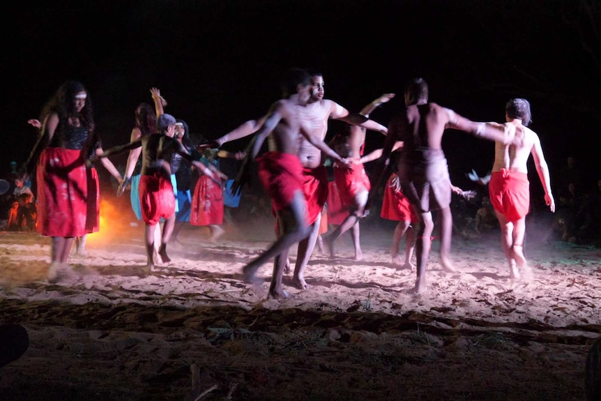 A group of Aboriginal dancers dance with their arms spread out.