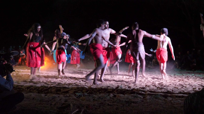 A group of Aboriginal dancers dance with their arms spread out.