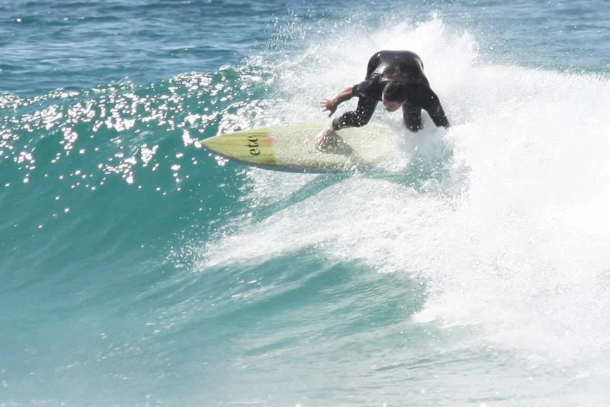 Surfer doing a turn on shoulder height wave riding a wooden eco board