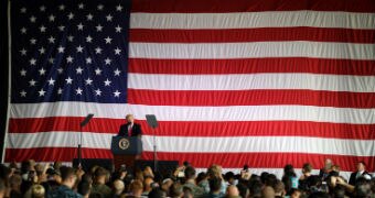 Donald Trump stands in front of a giant US flag, addresses US troops at a naval base.