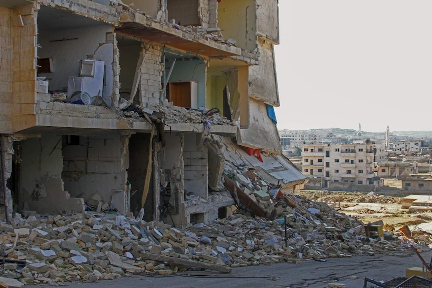 You view a bombed-out building shell with bricks strewn on the footpath, while you see a relatively intact city centre behind it