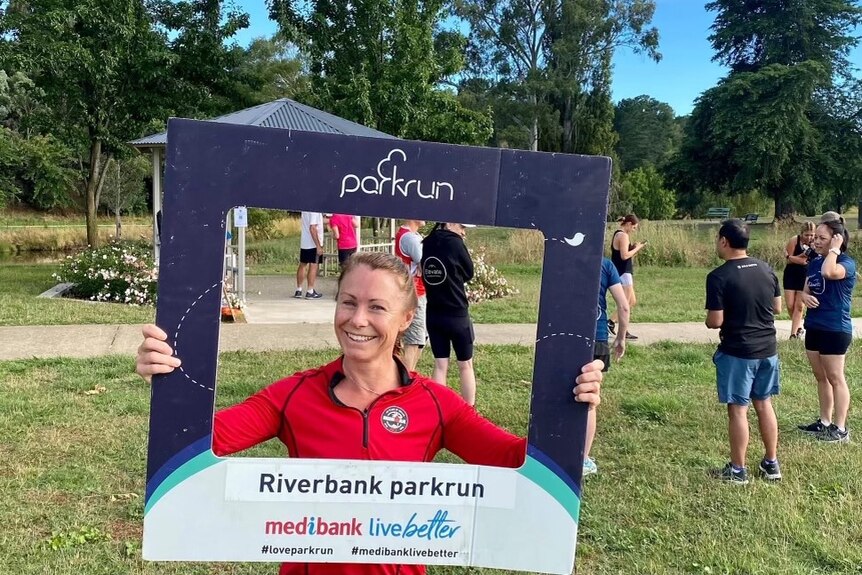 Sarah Watson holds a parkrun photo frame around her and smiles.