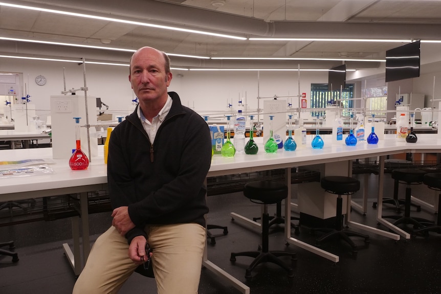 Man sitting on stool next to a row of test tubes 