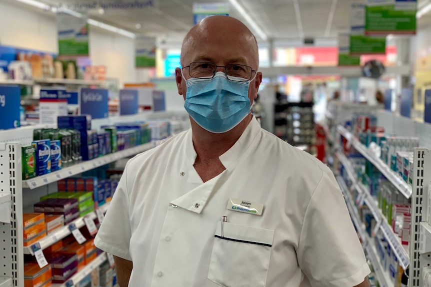 A male chemist wears a mask and looks to the camera in a pharmacy in Ararat