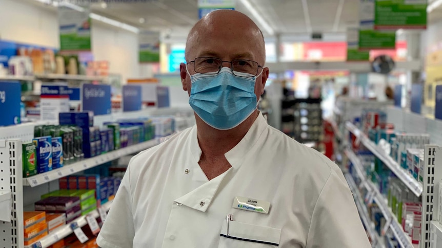 A male chemist wears a mask and looks to the camera in a pharmacy in Ararat