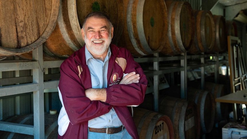 Mid shot of older man standing in front of port barrels with folded arms and smiling