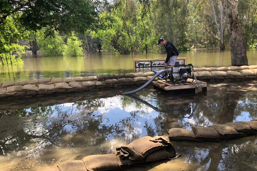 A man looking down at water pump in front of a flooded area