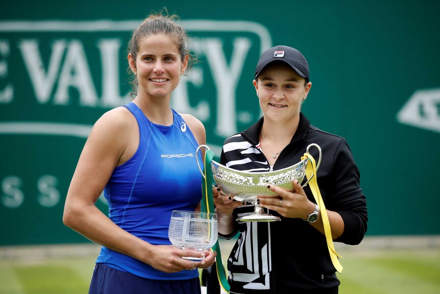 Two smiling tennis players hold their trophies after the final of a tournament.